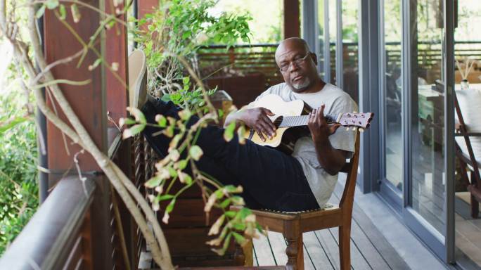 深思熟虑的非洲裔美国老人坐在阳台上弹吉他