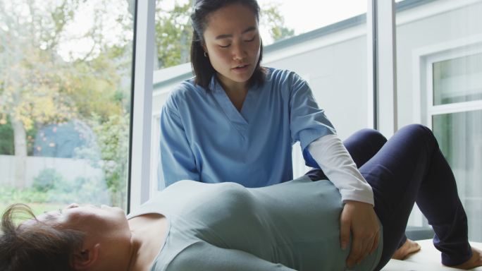 亚洲女性理疗师在手术中治疗躺在检查床上的女性病人