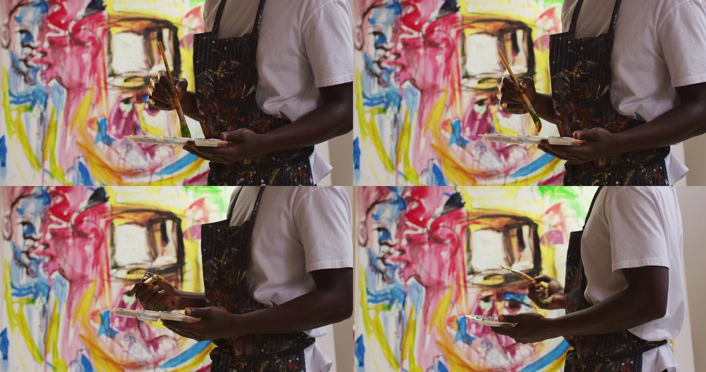 中间部分的非裔美国男性艺术家穿着围裙在画布上画在艺术工作室