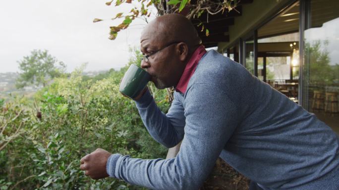 非裔美国老人站在阳台上喝咖啡，看风景