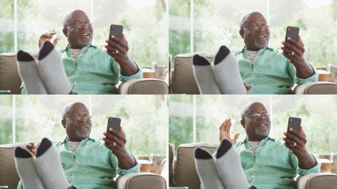 快乐的非洲裔美国老人坐着与脚与智能手机视频通话和挥手