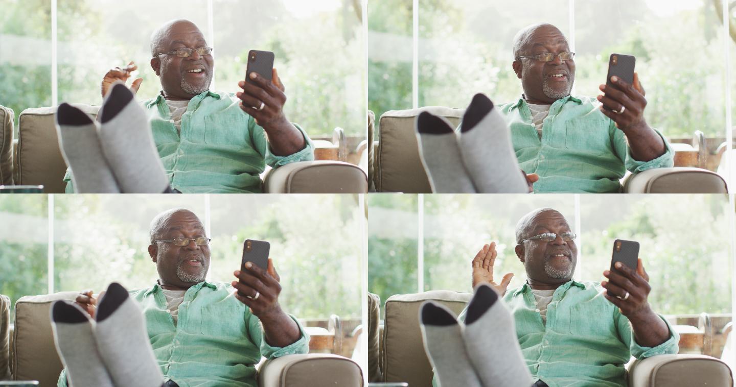 快乐的非洲裔美国老人坐着与脚与智能手机视频通话和挥手