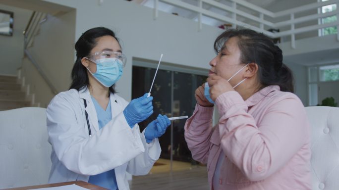 亚洲女护士戴口罩在医院对女患者进行covid - 19拭子检测