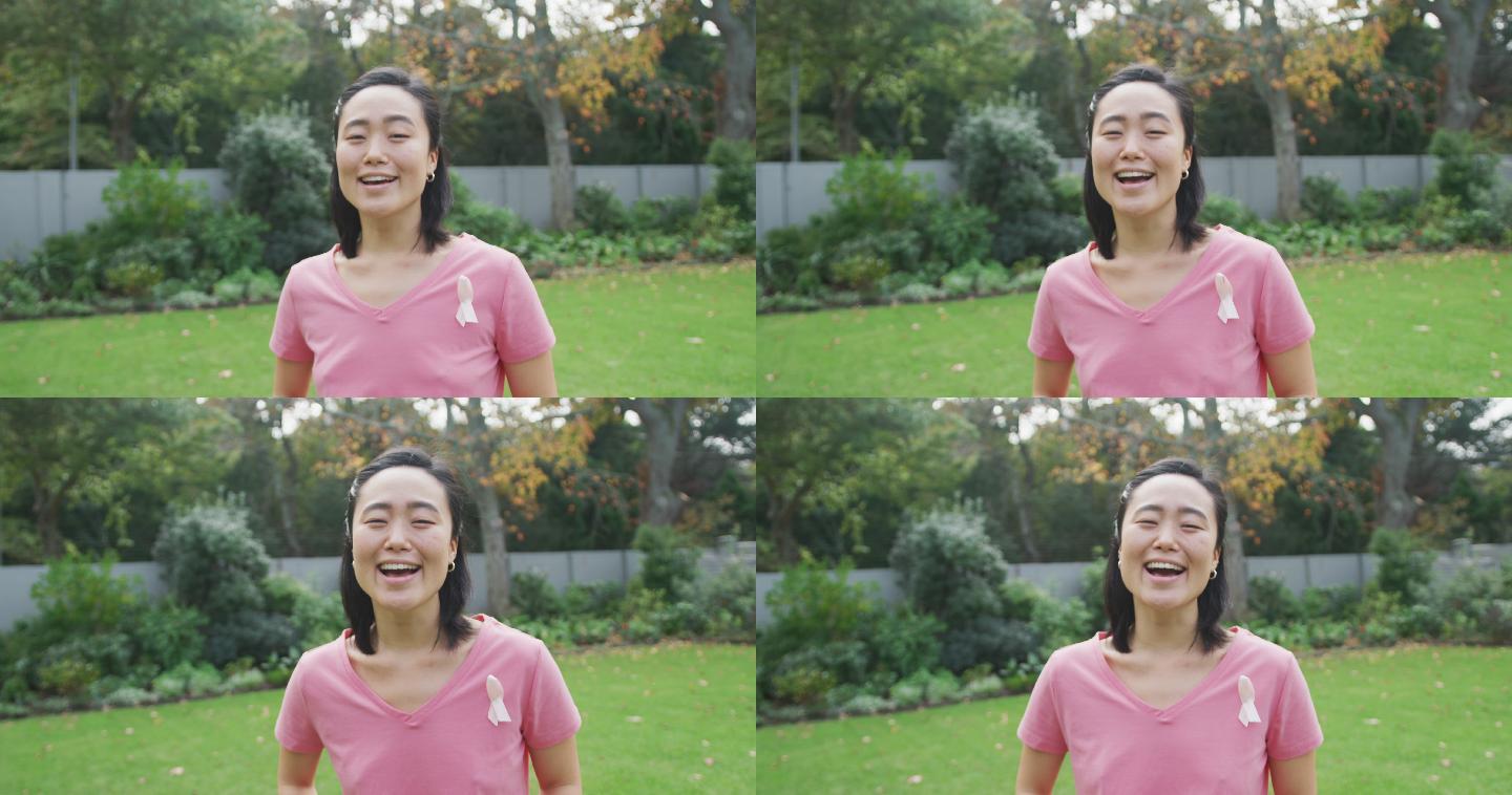 快乐的亚洲妇女肖像，穿着粉红色t恤和癌症丝带，站在花园笑