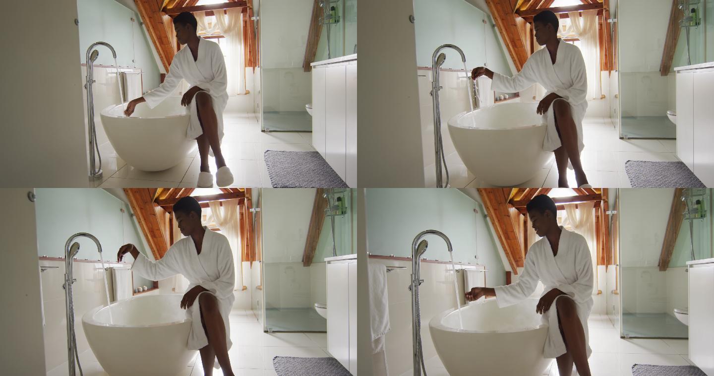 非裔美国人迷人的女人穿着白袍坐在浴缸上，准备沐浴