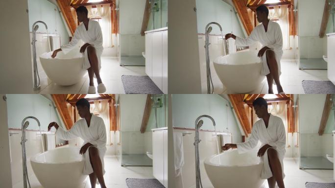 非裔美国人迷人的女人穿着白袍坐在浴缸上，准备沐浴