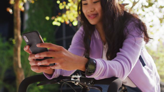 亚洲女子骑着自行车微笑着在公园里使用智能手机