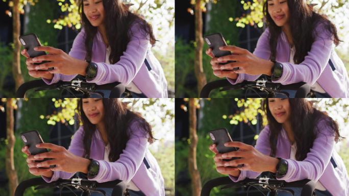 亚洲女子骑着自行车微笑着在公园里使用智能手机