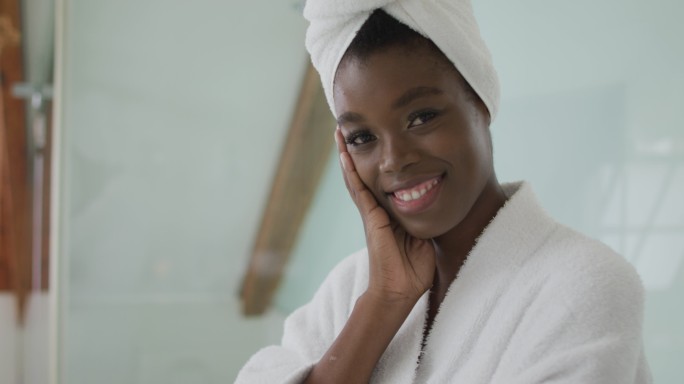 微笑的非裔美国人迷人的女人穿着长袍和头巾的肖像在浴室