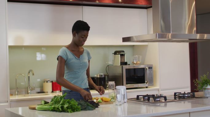 非裔美国人迷人的女人在厨房切蔬菜做冰沙