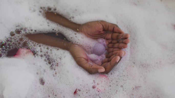 非裔美国美女的手用泡沫，盐和玫瑰花瓣沐浴