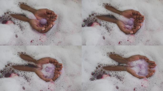 非裔美国美女的手用泡沫，盐和玫瑰花瓣沐浴