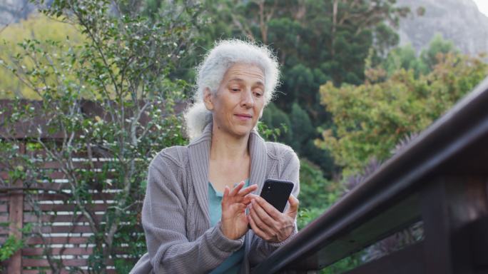 在阳台上使用智能手机的高级混血女性的肖像