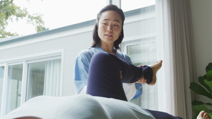 亚洲女理疗师在手术时扶着女病人躺在检查床上的腿
