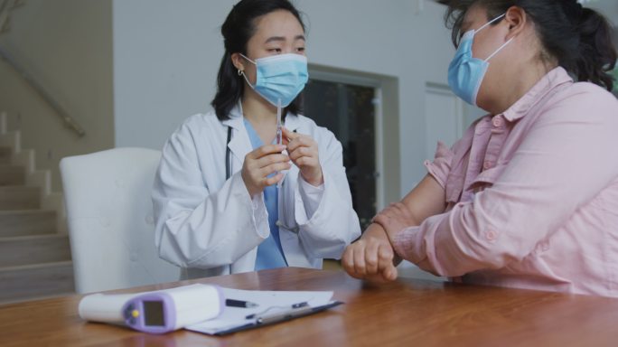亚洲女护士戴着口罩在医院为女性患者接种新冠疫苗