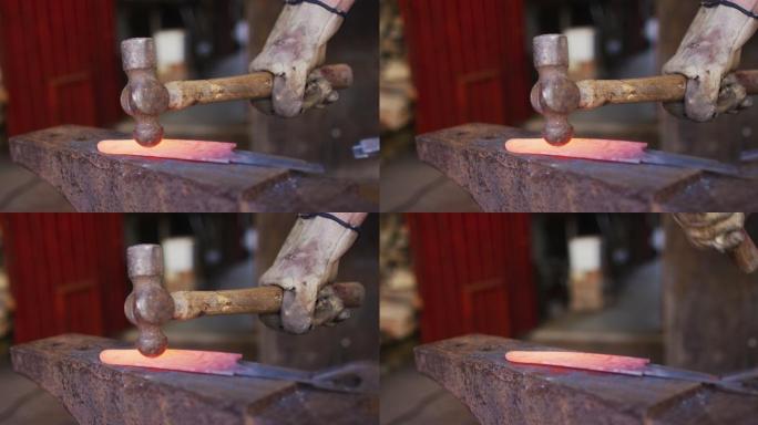 近距离拍摄车间里白人男制刀工手拿锤子和制刀