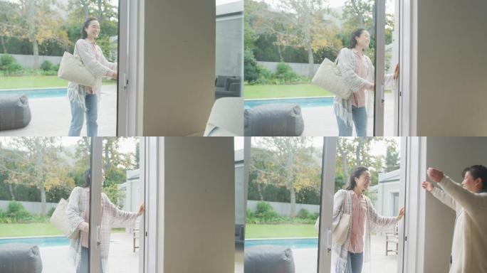 快乐的亚洲成年女儿到达和拥抱在门口的母亲从花园