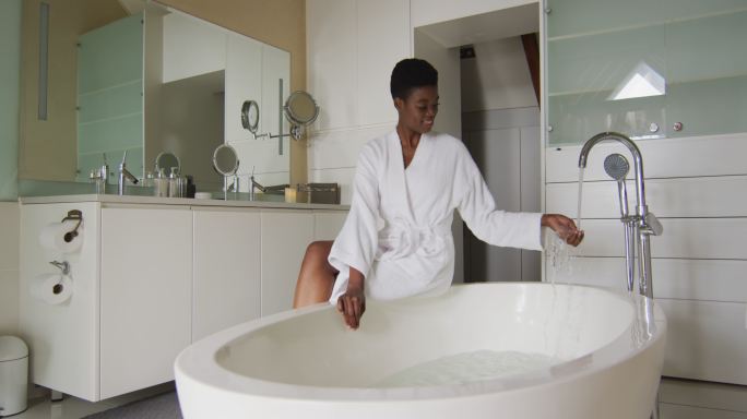 微笑的非洲裔美国人有吸引力的女人在白袍坐在浴缸，准备沐浴