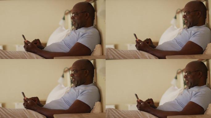 快乐的非洲裔美国老人坐在床上使用智能手机和微笑