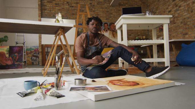微笑的非裔美国男性艺术家肖像穿着围裙在画布上画在艺术工作室