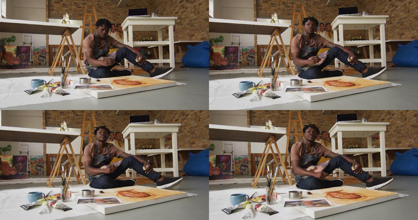 微笑的非裔美国男性艺术家肖像穿着围裙在画布上画在艺术工作室