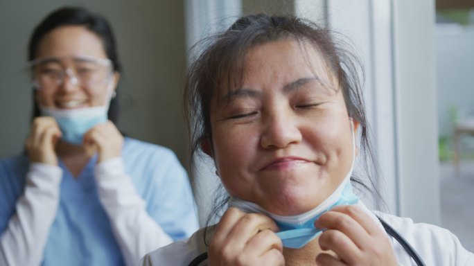 亚洲女护士和病人的肖像戴口罩，降低口罩和微笑对相机