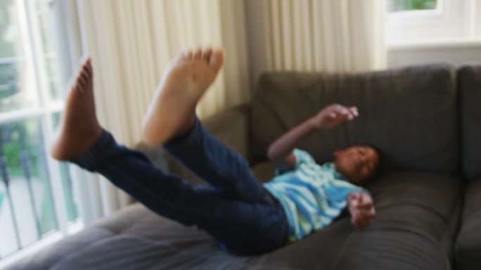 微笑的非洲裔美国男孩在家里的沙发上跳来跳去