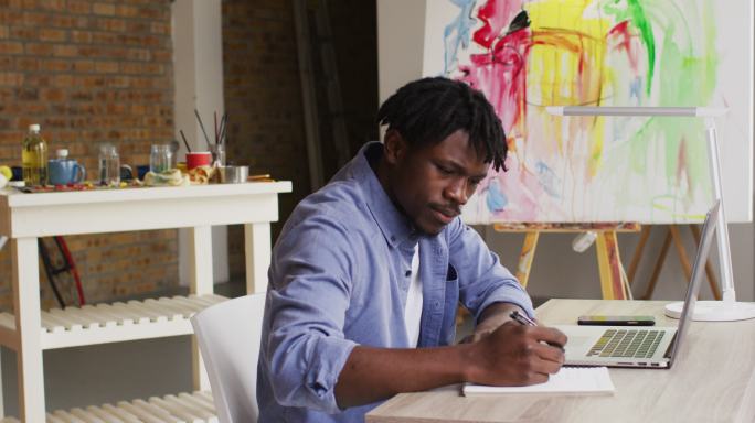 非裔美国男艺术家在艺术工作室的桌子上做笔记