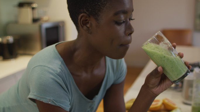 微笑的非洲裔美国人迷人的女人在厨房喝自制的冰沙的肖像