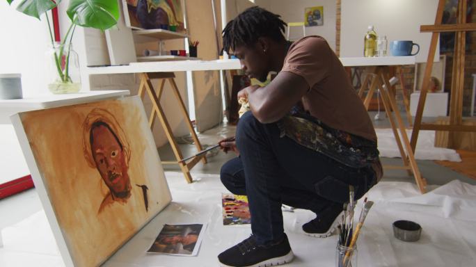 侧视图的非裔美国男性艺术家穿着围裙在画布上画在艺术工作室