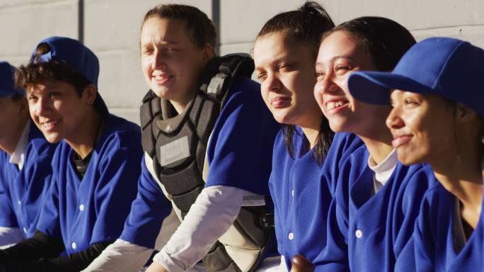 快乐的女棒球选手们坐在板凳上，微笑着听教练讲课