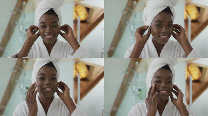 微笑的非洲裔美国人迷人的女人把毛巾放在头上，在浴室里看着镜子