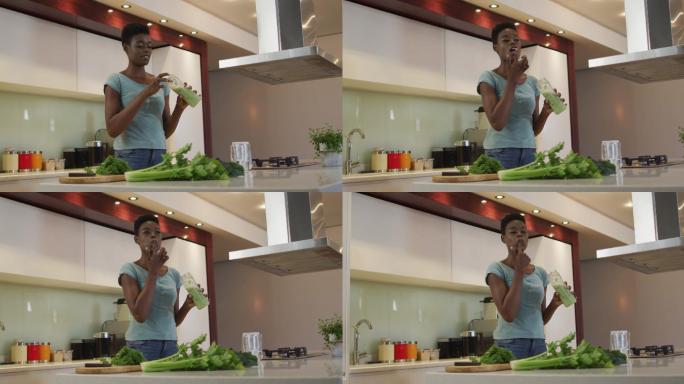 微笑的非洲裔美国人迷人的女人品尝自制冰沙在厨房