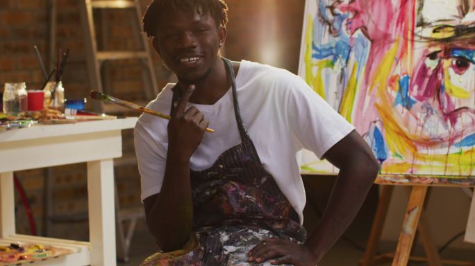 非裔美国男性艺术家的肖像穿着围裙拿着油漆刷微笑在艺术工作室