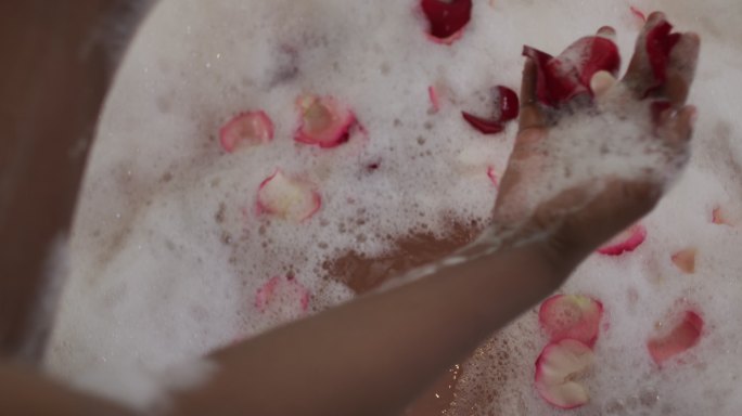 非裔美国美女的手用泡沫和玫瑰花瓣沐浴
