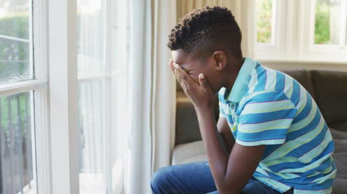 压力大的非裔美国男孩坐在家里的沙发上看着窗外