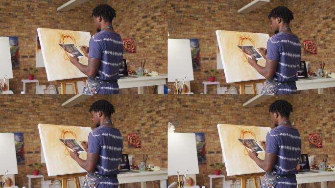 非裔美国男性画家从照片在画布上绘画在艺术家工作室