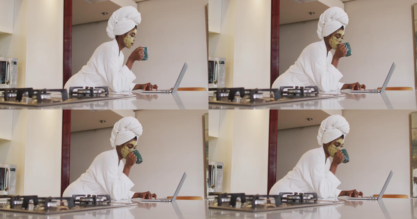 非裔美国人有吸引力的女人用面膜喝咖啡和使用笔记本电脑在厨房