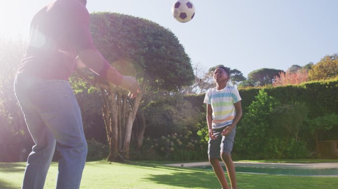 在一个阳光明媚的日子里，美国黑人爸爸和儿子一起在花园里踢足球