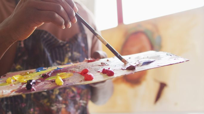 男艺术家身穿围裙，在画室里用笔刷在调色板上调色