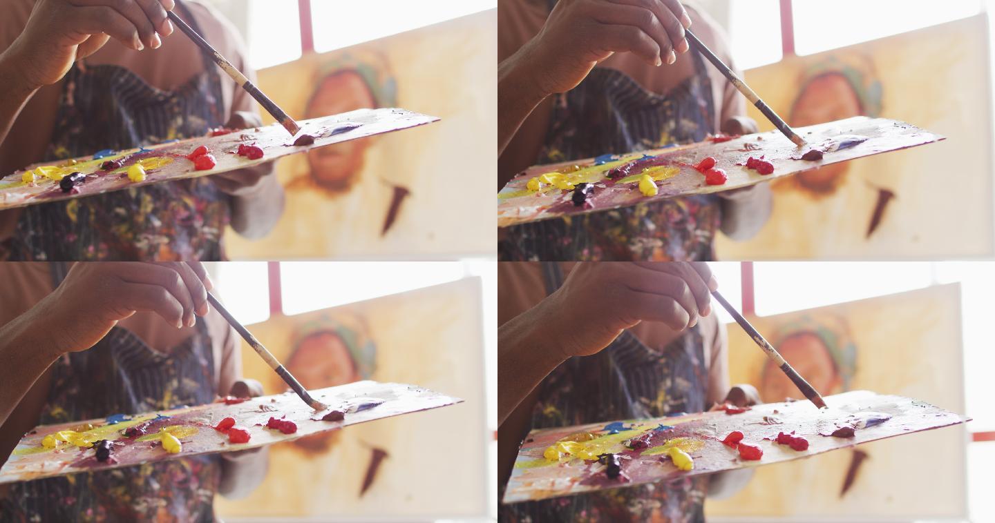 男艺术家身穿围裙，在画室里用笔刷在调色板上调色