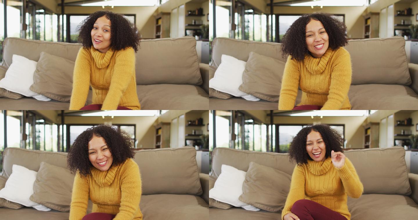 快乐的混血妇女坐在客厅的沙发上，挥手和微笑在视频通话