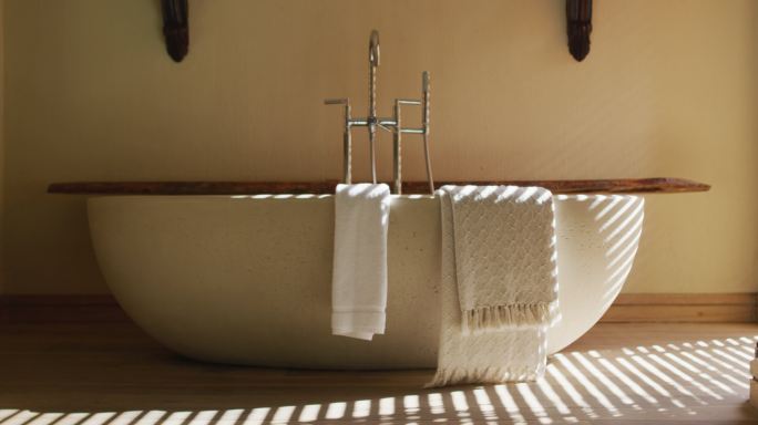 椭圆形白色浴缸在最小的现代浴室，阳光透过百叶窗