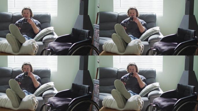 快乐的白人残疾人坐在客厅的沙发上用智能手机喝咖啡