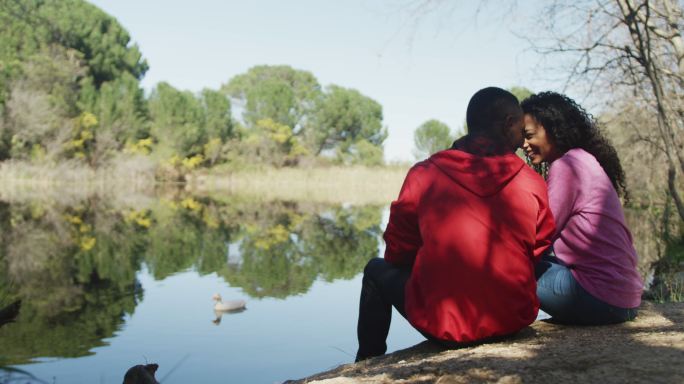 微笑的不同夫妇拥抱和坐在湖边的乡村