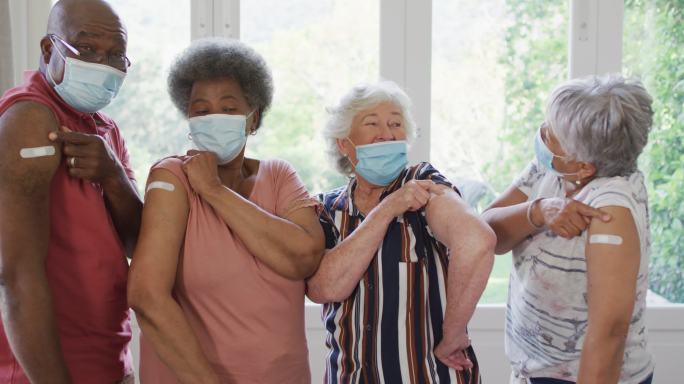 一群戴着口罩的老年人在家里展示他们接种过疫苗的肩膀