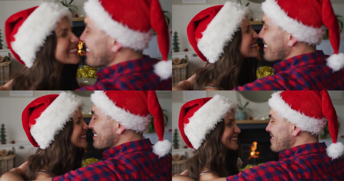 幸福的白种人夫妇戴着圣诞老人帽坐在沙发上，互相摩擦
