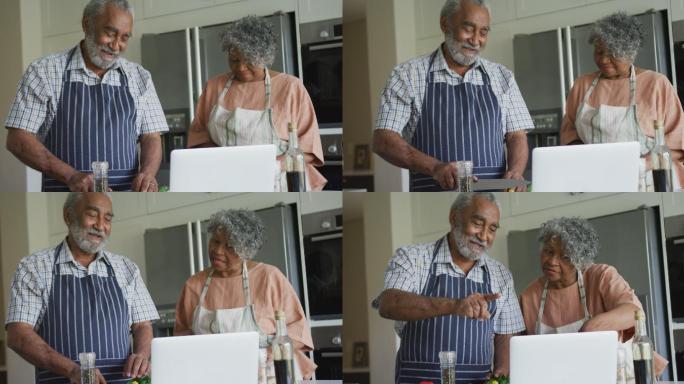 快乐的非裔美国老年夫妇用笔记本电脑一起做饭