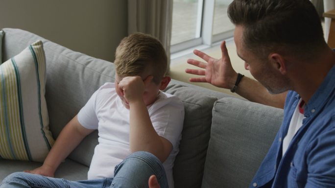 一个白人父亲坐在客厅里和他伤心的儿子聊天