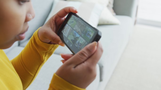 快乐的非裔美国胖女人坐在沙发上，在客厅用智能手机